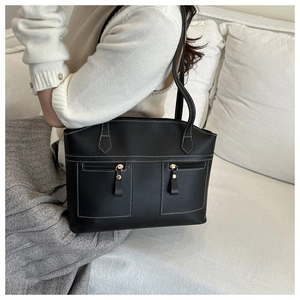 Detail of black leather tote bag featuring contrast white stitching and gold hardware accents