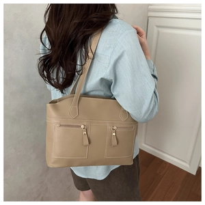 Model wearing a khaki PU leather shoulder bag with symmetrical zippers in a minimalist room