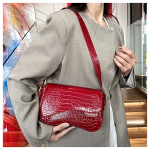 Detail of red crocodile texture underarm bag with asymmetrical curved design and glossy finish