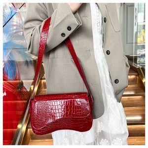 Detail of dark red crocodile pattern shoulder bag with wavy bottom and flap closure