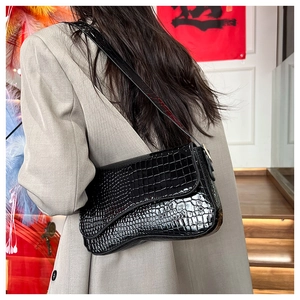 Detail of black faux crocodile leather underarm bag worn on shoulder by a model