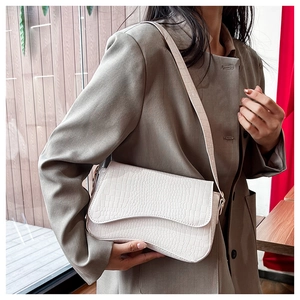 Detail of white crocodile-embossed leather flap bag worn as a shoulder bag on model
