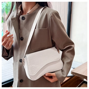 Detail of white crocodile pattern shoulder bag with unique curved flap on female model