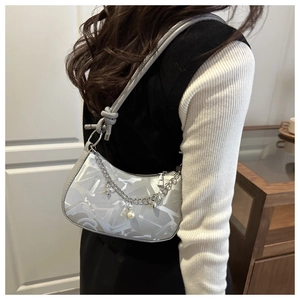 Detail view of silver crescent bag with monogram print, metal chain, and pearl pendant