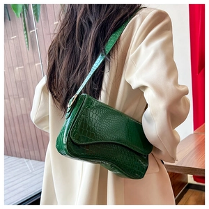 Detail of dark green crocodile pattern underarm bag with glossy finish and gold hardware