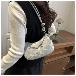 Close-up of silver-grey chain bag with abstract print and pearl charm on a shoulder