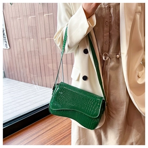 Detail of green crocodile texture faux leather baguette bag with curved bottom design