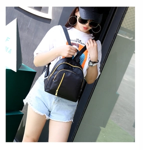 Close-up showing a black mini nylon backpack with stylish gold metal zippers on a model
