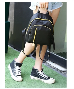 Mini black nylon backpack with yellow zipper detail shown on a person for scale