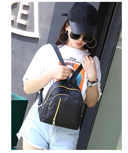 Close-up of black nylon mini backpack with golden metal zippers on a stylish model