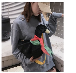 Close-up of black plush duck crossbody bag with red checkered bow and yellow strap