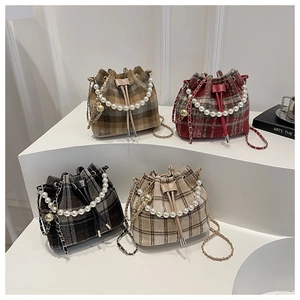 Close-up of four plaid tweed bucket bags with pearl handles and chain straps in soft light