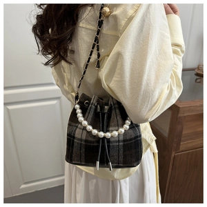 Detail of vintage plaid bucket bag with pearl handle and metal chain strap on shoulder