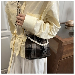 Detail of checkered bucket bag with pearl handle and metal chain strap on model
