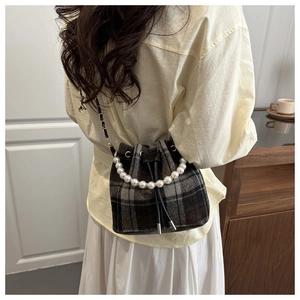 Detail of vintage plaid bucket bag featuring pearl handle and woven chain strap on model
