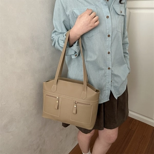 Stylish khaki leather tote bag with dual front zippers worn by a model in casual outfit