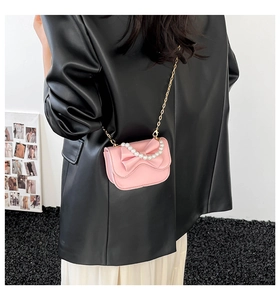Detail of pink PU leather square bag with bow and pearl handle worn as crossbody