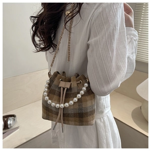 Detail of tweed bucket bag featuring a pearl handle and metal chain strap on a model