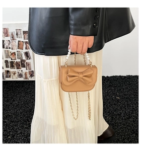 Detail of camel mini bag featuring bow design, pearl handle, and gold metal chain strap