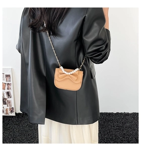 Detail view of mini tan shoulder bag with pearl handle and bow on a leather jacket