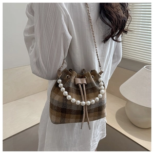 Detail of plaid bucket bag with pearl handle and drawstring closure shown on shoulder