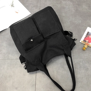 Detail of black canvas tote bag showing front utility pockets and adjustable shoulder strap