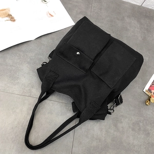 Detail of a black canvas tote bag with front square pockets and reinforced woven handles