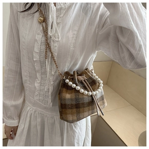 Detail of brown plaid bucket bag featuring pearl handle and chain strap on a dress