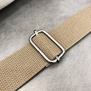 Macro view of beige canvas shoulder strap with dark gray metal adjustable buckle