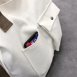 Detail of white canvas tote featuring an outer pocket with a smartphone to show depth