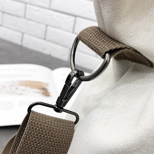 Detail shot of the black metal lobster clasp and D-ring on the white canvas shoulder bag