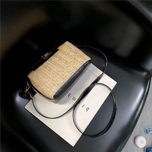 Close-up of beige woven straw texture and black leather trim on a crossbody bag