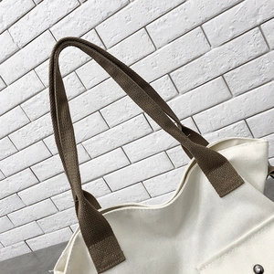 Detail of canvas tote bag showing cross-stitched dark brown handles and metal rivet