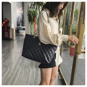 Detailed view of black quilted tote bag featuring a golden deer charm and chain straps