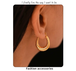 Close-up of golden U-shaped earrings with unique honeycomb texture on model ear