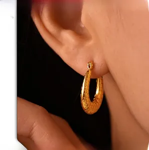 Detailed view of U-shaped gold earrings with hexagonal honeycomb texture on ear