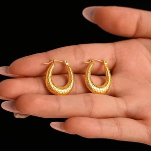U-shaped golden earrings with fish scale texture held by hand on black background