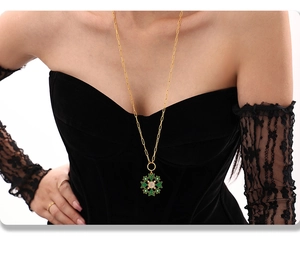 Golden necklace with green snowflake pendant worn by model against black clothing