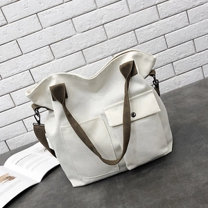 Detail of cream canvas tote bag showing front pockets and adjustable brown strap