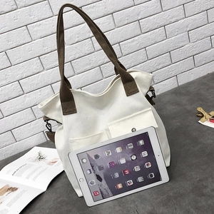 Detail of cream canvas tote bag featuring brown straps and double front pockets