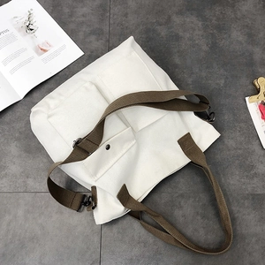 Detail of off-white canvas tote bag featuring brown woven straps and three functional pockets