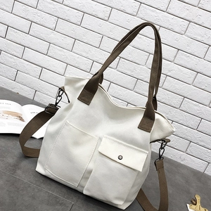 Detailed view of white canvas tote bag with brown straps and large front pockets