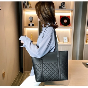 Detailed view of large black quilted leather tote bag worn on shoulder in cozy room
