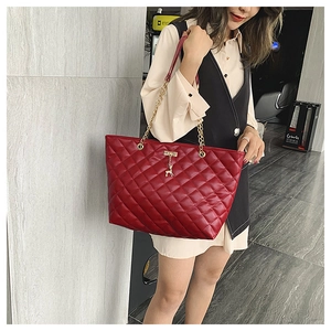 Close-up of red quilted tote bag with gold deer pendant and chain strap on a model