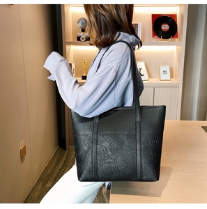 Detailed view of black tote bag featuring embossed rose floral texture and slim shoulder straps