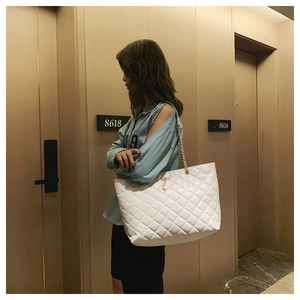 White quilted tote bag with gold chain strap shown on model in a stylish hotel setting