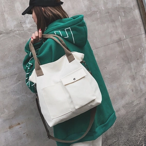 Detail of off-white canvas tote bag with brown adjustable strap and functional front pockets