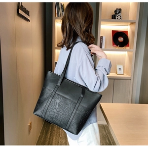 Detail of black leather tote bag featuring 3D rose embossing and dual shoulder straps