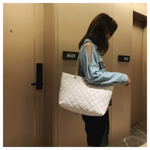 Detailed close-up of a white quilted leather tote bag with elegant gold chain strap