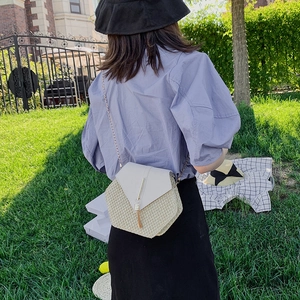 Straw chain crossbody bag with tassels and hexagonal design shown in outdoor setting